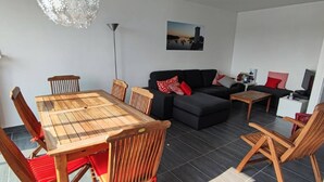 A modern living room with a wooden dining table, black sofa, and wooden chairs. - La Nantaise de la mer Saint Hilaire de Riez (SAINT HILAIRE DE RIEZ)