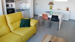 Ett modernt vardagsrum med en gul soffa, en matplats med två stolar och ett kök i bakgrunden.