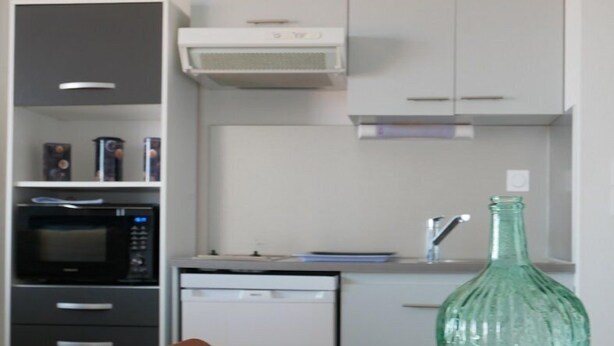 Ett modernt kök med mikrovågsugn, ugn och diskmaskin. En grön glasflaska står på bordet.