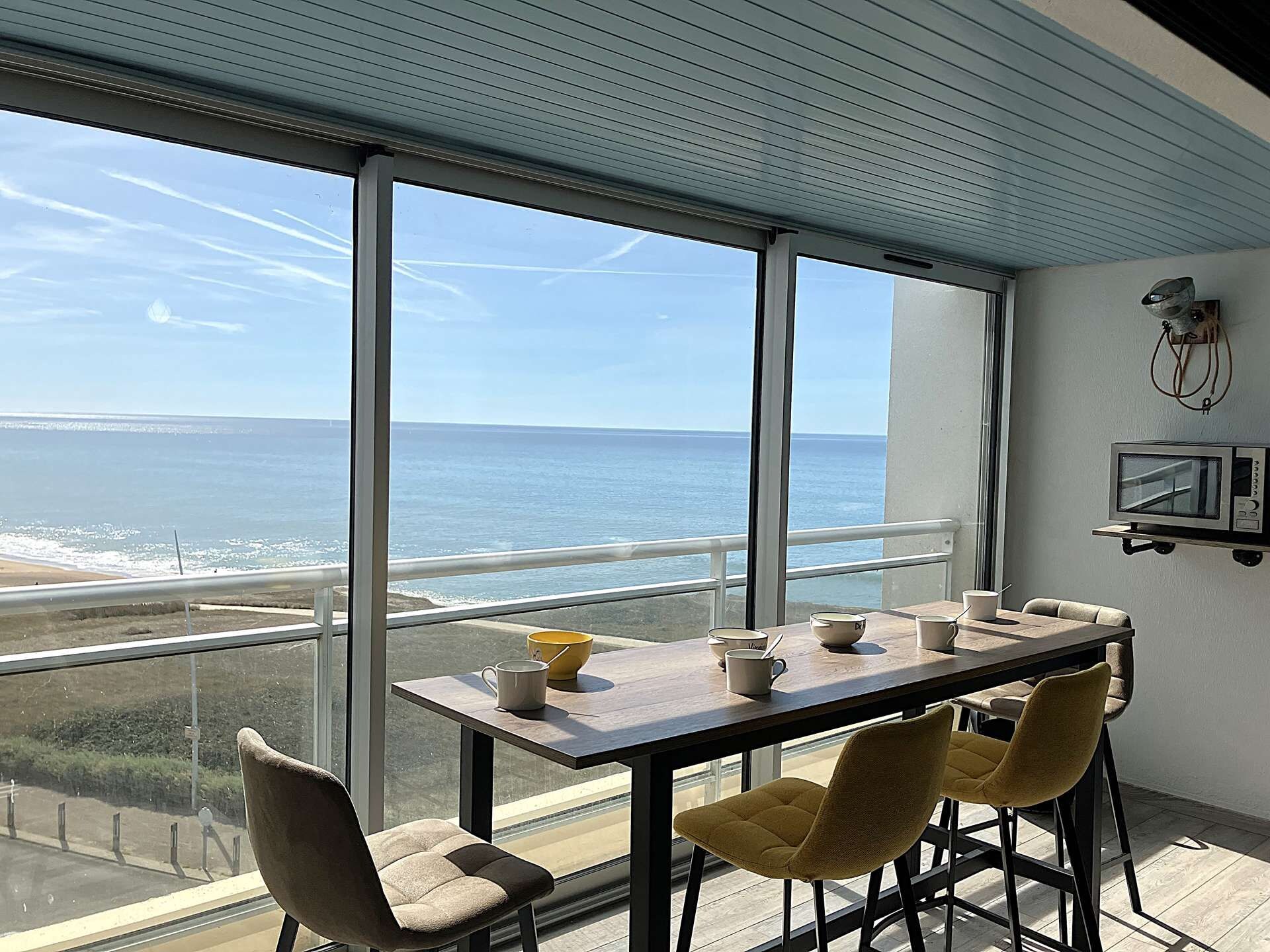 A dining area with a view of the ocean, a table with chairs, and a television mounted on the wall.