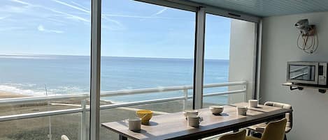 A dining area with a view of the ocean, a table with chairs, and a television mounted on the wall.