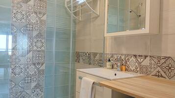 Une salle de bain dotée d’une douche à parois de verre, d’un lavabo avec un plan de travail en bois et de carreaux décoratifs sur les murs.