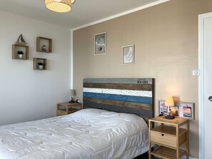 Une chambre à coucher comprenant un lit, deux tables de chevet, une commode, une tête de lit ornée d’un motif peint et des œuvres d’art accrochées au mur.