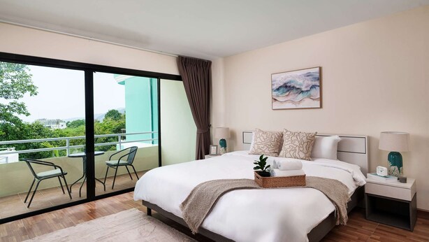 Un dormitorio con una cama grande, una mesita de noche, una silla, una ventana con vistas a zonas verdes y un cuadro en la pared.