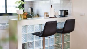 Cocina moderna con barra que incluye dos taburetes negros, una planta en maceta y una cafetera.