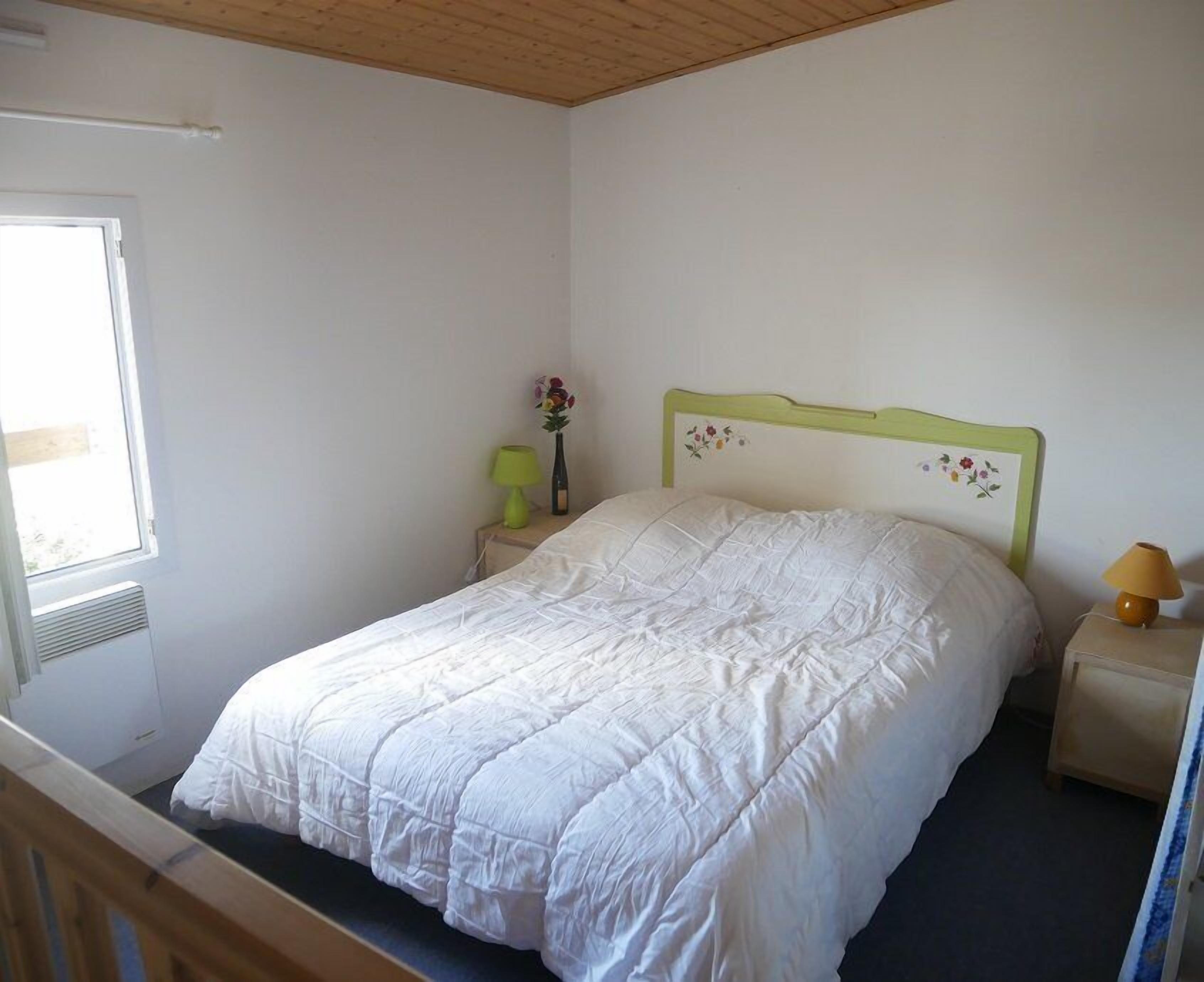 Et soveværelse med en enkelt seng, et natbord med en lampe og et vindue med udsigt til det fri.
