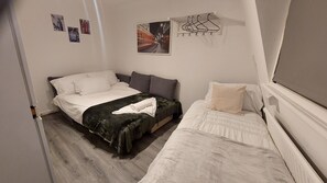 A small, neatly arranged bedroom with two single beds, a small table, and a wall-mounted drying rack.