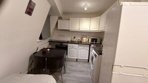 A compact kitchen with white cabinets, a microwave, a sink, and a washing machine. - 2-bed Apartment Sleeps 7 With Wi-fi (London)