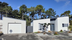 A modern building with two garage doors, a small garden with a tree, and a clear blue sky. - La moderna de la pège - Saint hilaire de Riez (SAINT HILAIRE DE RIEZ)