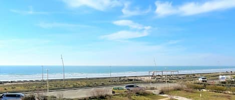 A coastal road with a view of the ocean, a parking area, and a pedestrian path.