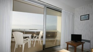 Ein Balkon mit Tisch und Stühlen, ein Fernseher auf einem kleinen Tisch und Blick auf das Meer.