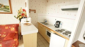 Eine kompakte Küche mit Spüle, Herd und kleinem Kühlschrank. Es gibt eine Holz Arbeitsplatte und einen Essbereich mit Tisch und Stühlen.