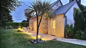 A stone house with a paved patio and a small garden with a palm tree. - Le Cottage d'Etaville (Sottevast)