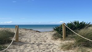 A sandy beach path leading to the ocean with a rope barrier and some vegetation. - Le Cottage d'Etaville (Sottevast)