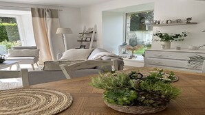 A modern living room with a wooden dining table, a woven placemat, and a potted plant centerpiece. - Le Cottage d'Etaville (Sottevast)