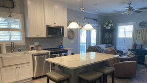 A modern kitchen with white cabinetry, stainless steel appliances, a central island with stools, and a dining area with a sofa and chairs. - Masters Rental, 7 miles from course, 6 bedrooms, southern charm (Evans)