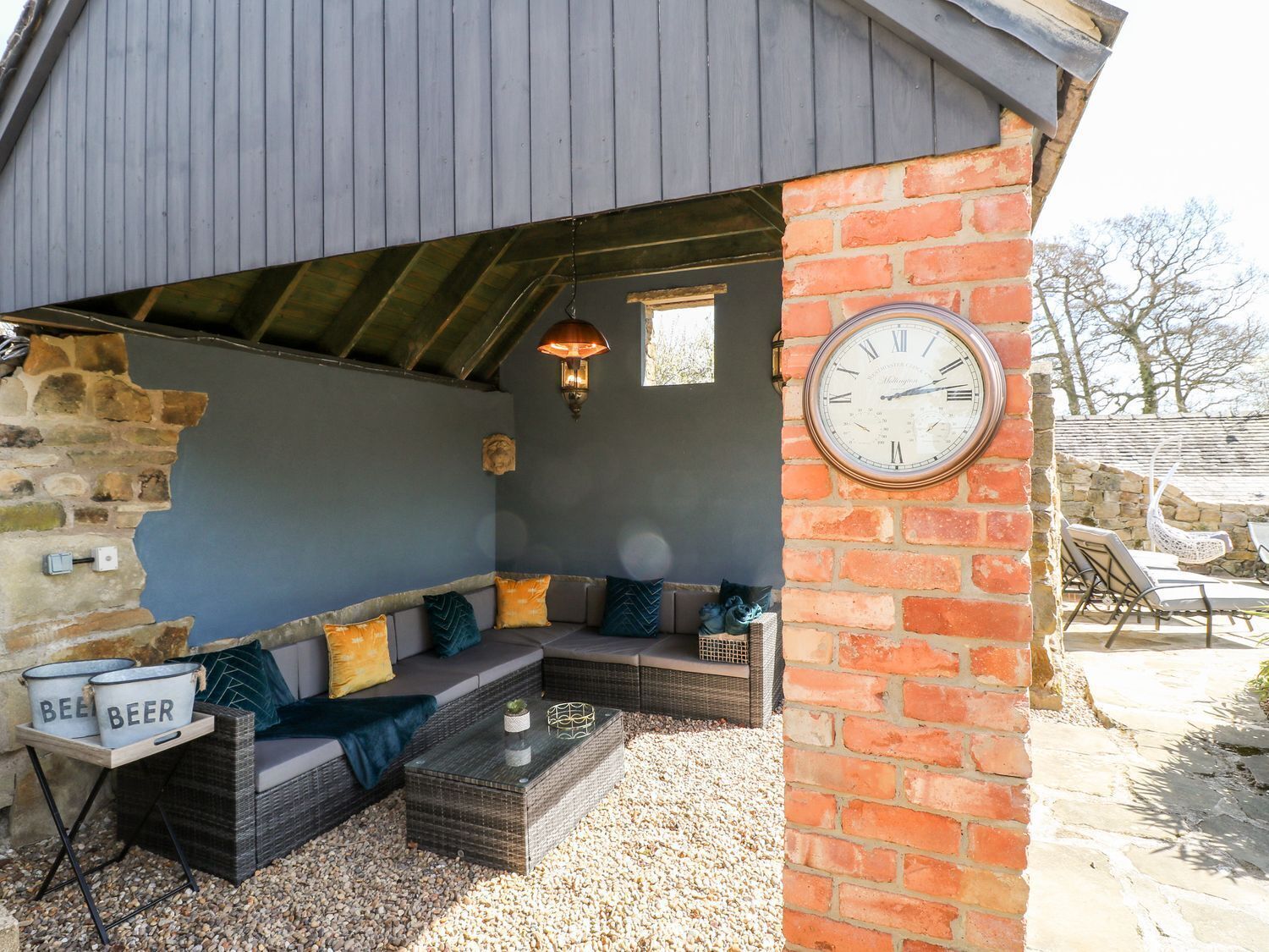 A cozy outdoor seating area with a stone wall, a clock, and a rustic ceiling.