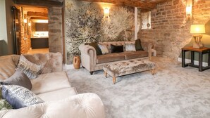 Ein gemütliches Wohnzimmer mit einer Couch, einem Hocker und einer Lampe auf einem Beistelltisch.