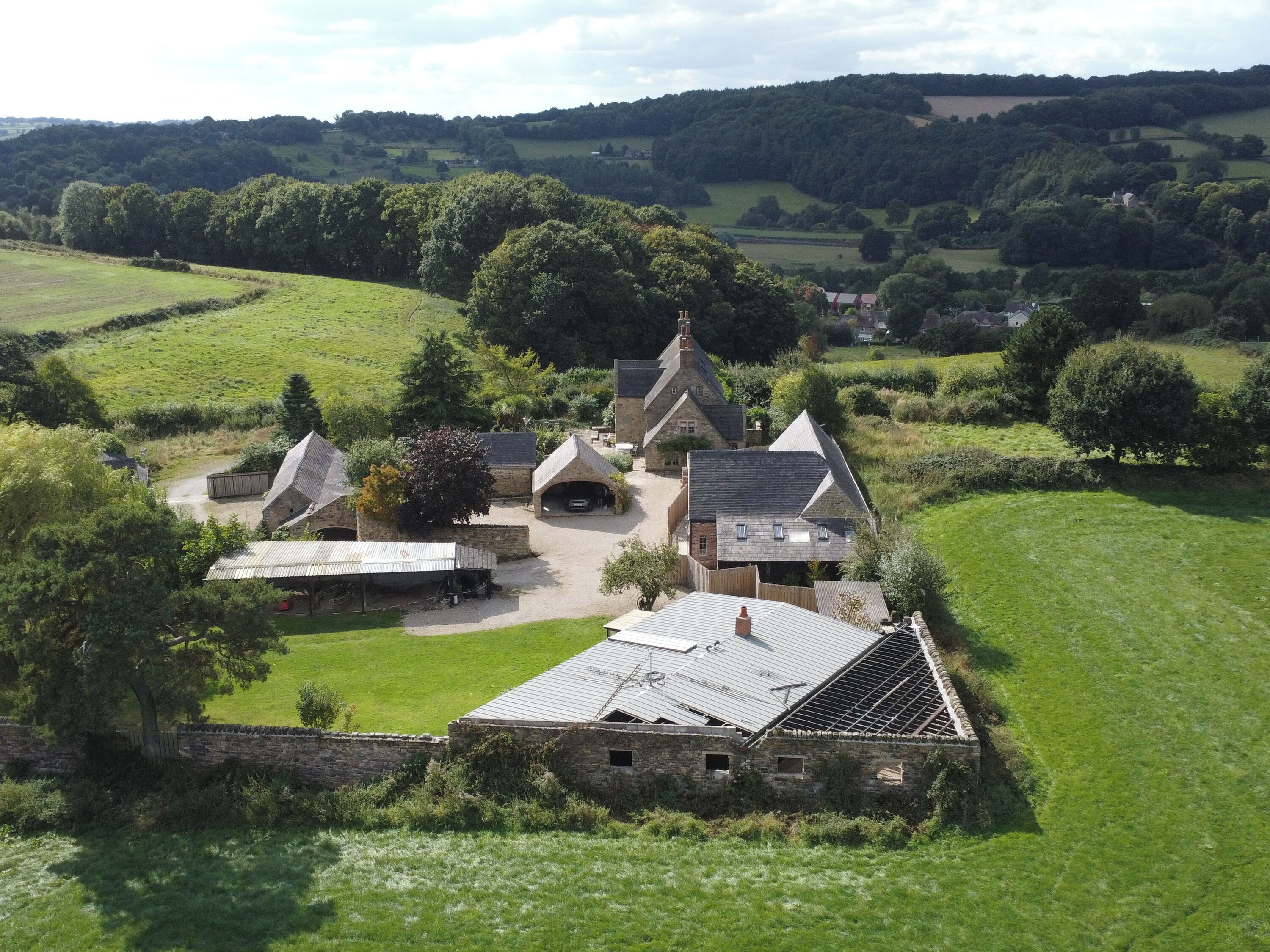 Un domaine rural comprenant plusieurs bâtiments, notamment une grande maison avec une cheminée imposante, des constructions plus petites et une pelouse bien entretenue.
