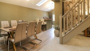 Un espace repas doté d’un plafond haut, de lucarnes et d’un escalier avec une rampe en bois.
