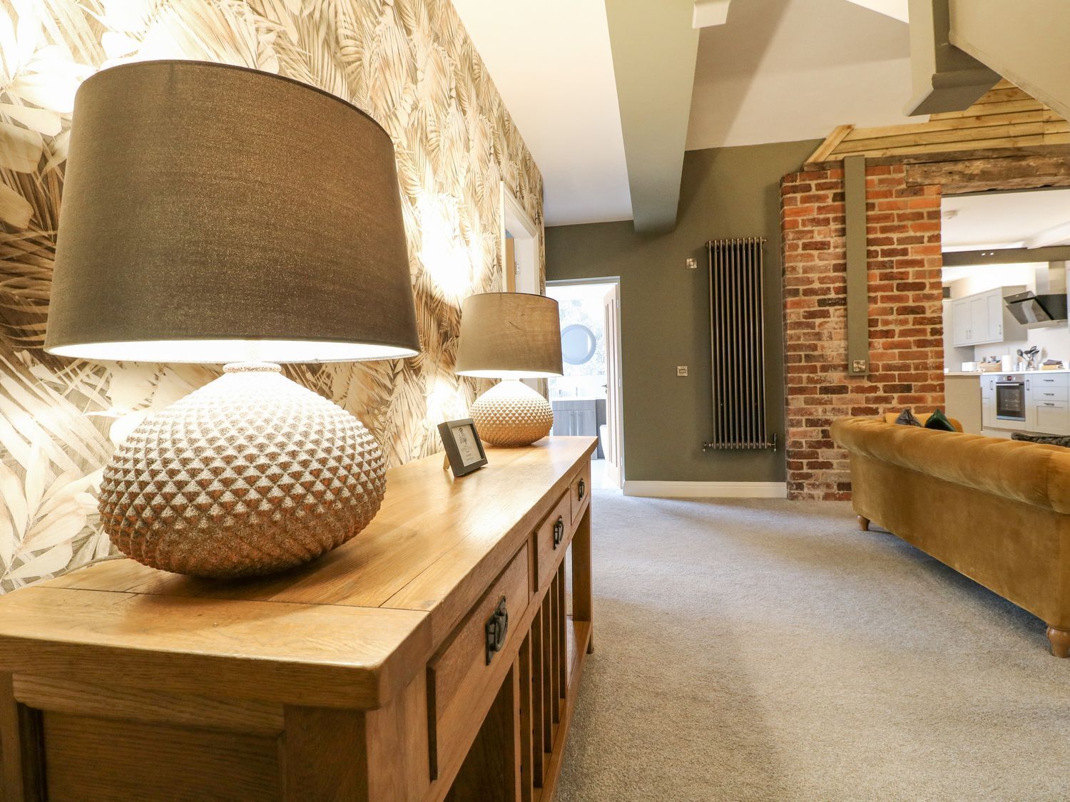 A cozy living room with a wooden coffee table, two lamps, a patterned cushion, and a brick wall.