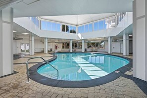 Une piscine intérieure offrant une vue dégagée sur le ciel grâce à de grandes fenêtres, et entourée d’une architecture moderne caractérisée par un motif géométrique sur le sol.