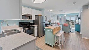 A modern kitchen with stainless steel appliances, a marble countertop, and a view to the living area. - Beachfront Gulf Views Fort Morgan Pool Sleeps 7! (Gulf Shores)