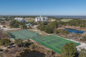 Ein Tennisplatz, umgeben von Bäumen, mit einem großen Gebäude im Hintergrund.