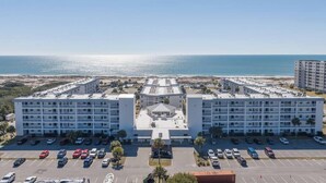 A multi-story hotel with a central courtyard, parking lot, and a view of the ocean. - Beachfront Gulf Views Fort Morgan Pool Sleeps 7! (Gulf Shores)