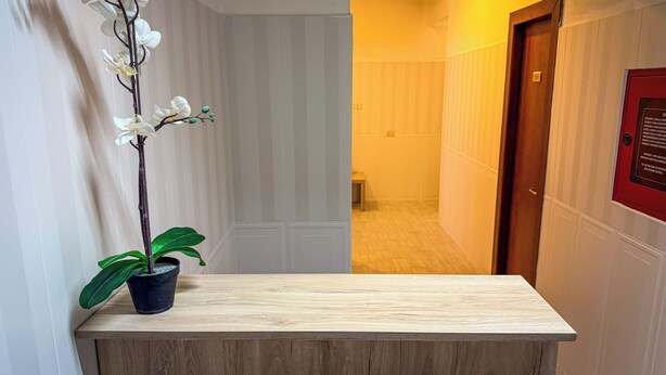 Un mostrador de recepción con una orquídea en maceta, una encimera de madera y un pasillo con una puerta y un cartel en la pared.
