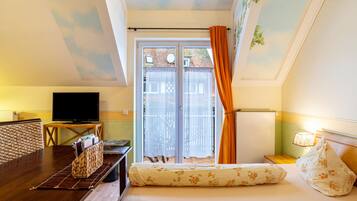 A bedroom with a bed, a TV, a desk, and a balcony with a view of the outside.