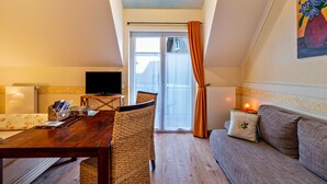 Une pièce chaleureuse avec une table à manger en bois, des chaises en osier, un canapé, un téléviseur et un balcon agrémenté de rideaux orange.
