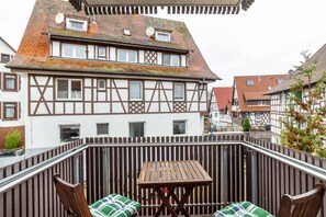 A traditional half-timbered house with a wooden deck, a table, and two chairs. - SCHUSTERjunge APARTHOTEL (Sasbachwalden)