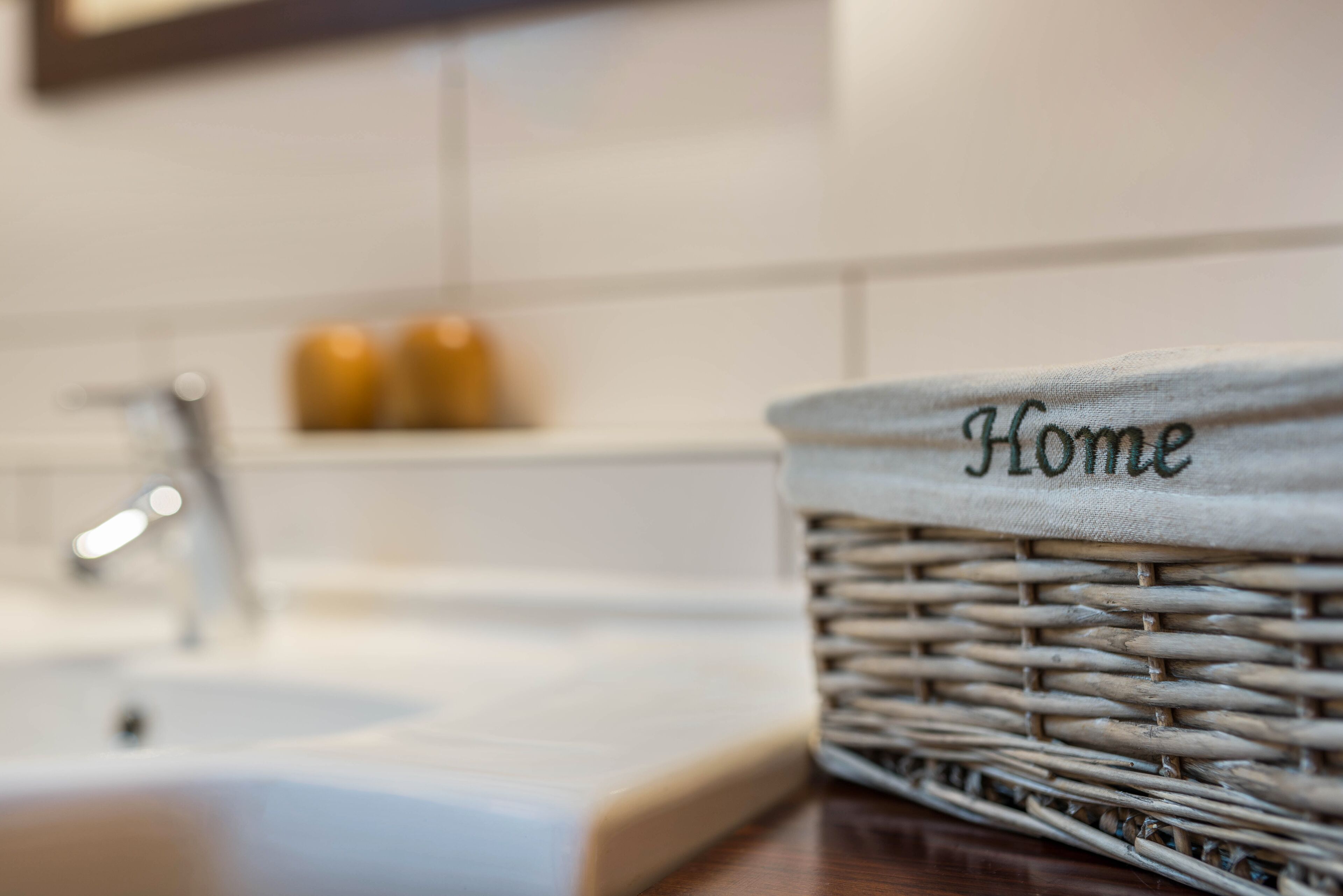 A wicker basket with the word "Home" on it, placed on a kitchen counter near a sink.
