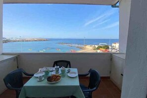 Un balcón con mesa lista para el desayuno, con vistas a la costa, un muelle y una playa.