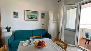 A room with a teal sofa, a dining table with a fruit bowl, and a painting on the wall. - Holiday apartment with sea view (San Teodoro)