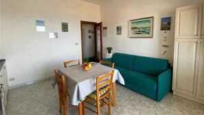 A dining area with a table set for two, a teal sofa, and a cabinet. - Holiday apartment with sea view (San Teodoro)