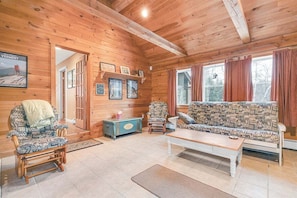 A wooden cabin interior with a sofa, chairs, a coffee table, and a fireplace.