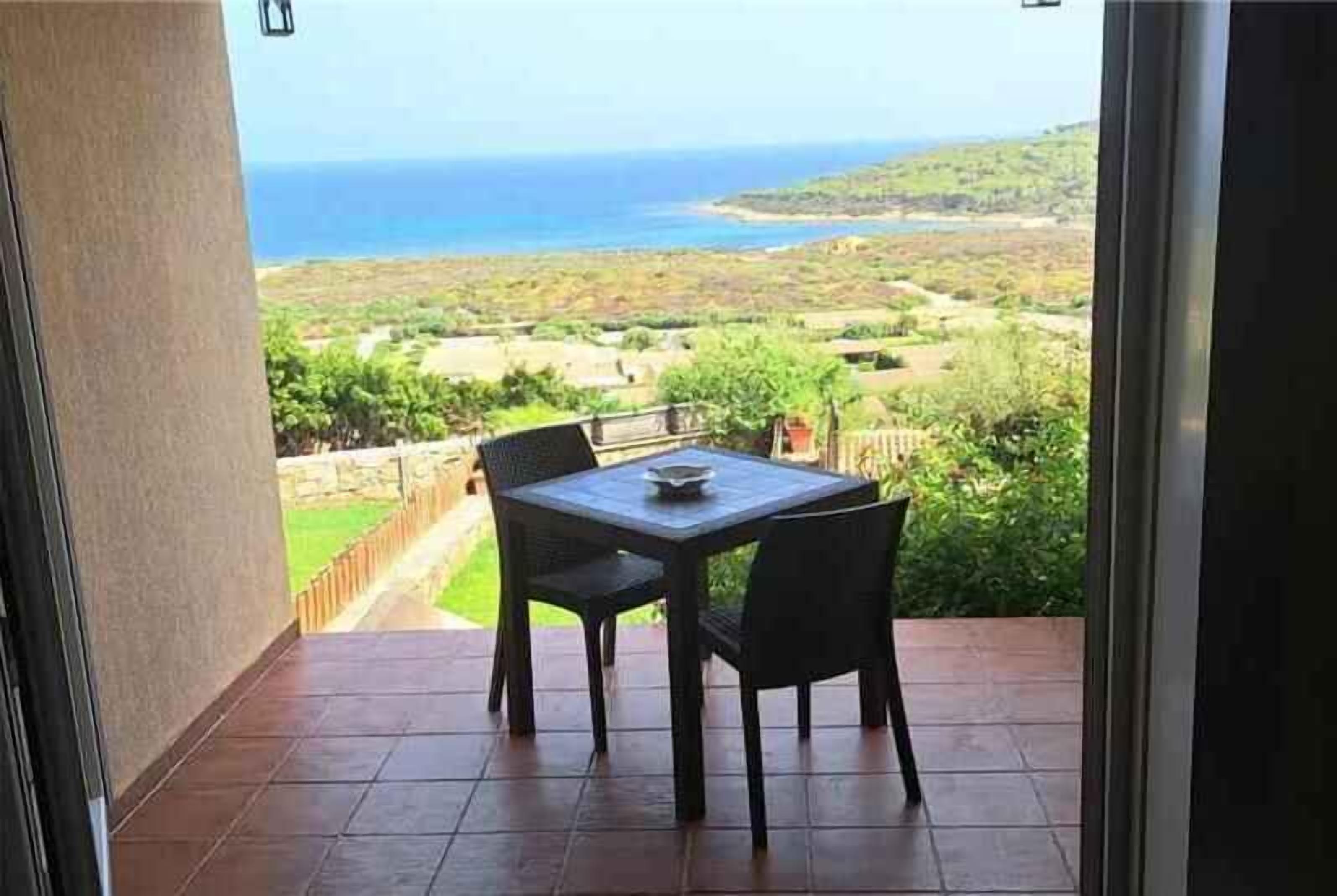 A balcony with a table and chairs, overlooking a coastal landscape.