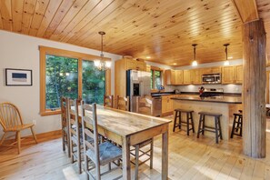 A wooden interior with a dining table, chairs, a refrigerator, a microwave, and a sink area.
