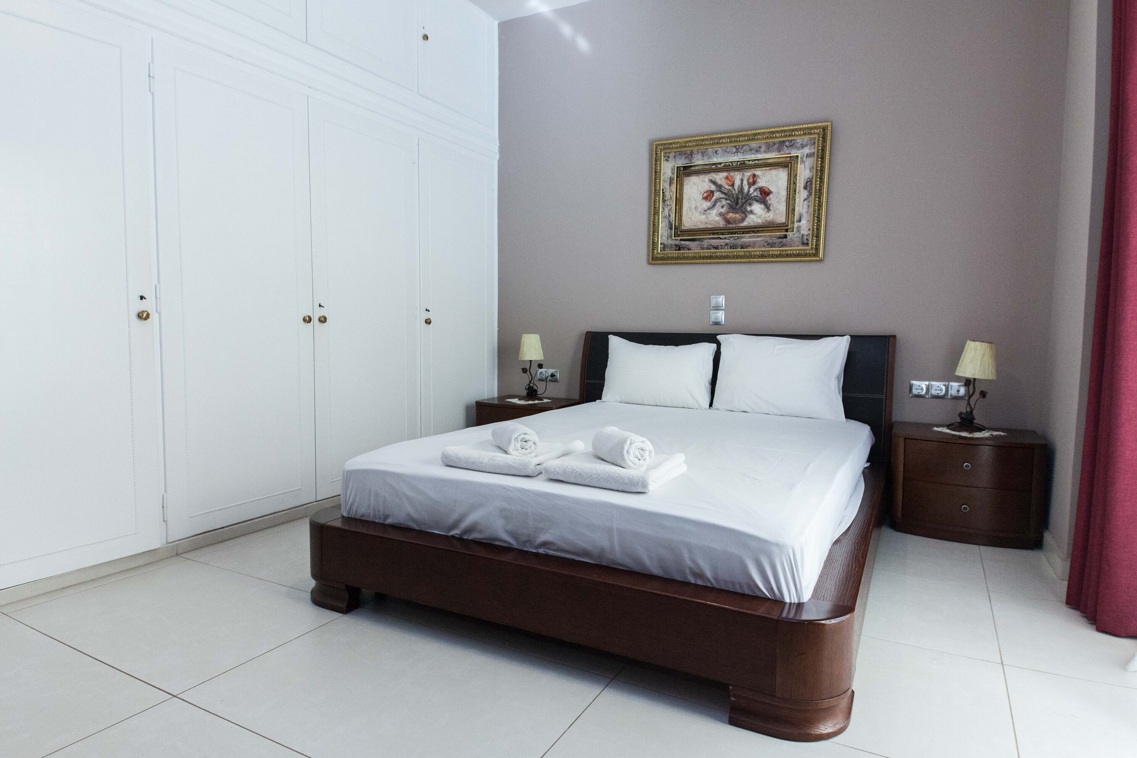 A neatly made bed with white linens and towels, a wooden headboard, and a nightstand with a lamp.