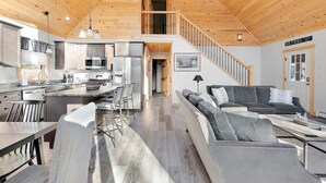 A modern interior with a kitchen, dining area, and living room, featuring wooden ceilings and a staircase.