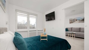 A modern bedroom with a bed, a TV mounted on the wall, and a window with blinds. - Functional Apartment in the Center | Close to the Sea and Balcony (Gdynia)