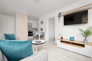 A modern living room with a sofa, a coffee table, and a TV mounted on the wall. There is a dining area with a table and chairs, and a kitchen in the background. - Functional Apartment in the Center | Close to the Sea and Balcony (Gdynia)