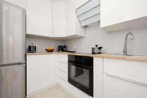 A modern kitchen with white cabinets, a stainless steel refrigerator, a black oven, and a wooden countertop. - Functional Apartment in the Center | Close to the Sea and Balcony (Gdynia)