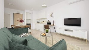 A modern living room with a green sofa, a dining area with a wooden table, and a kitchen in the background. - Charming Apartment with Balcony | Close to Chopin Airport (Warszawa)