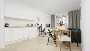 A modern kitchen with white cabinets, a dining area with a wooden table and chairs, and a large window with curtains.