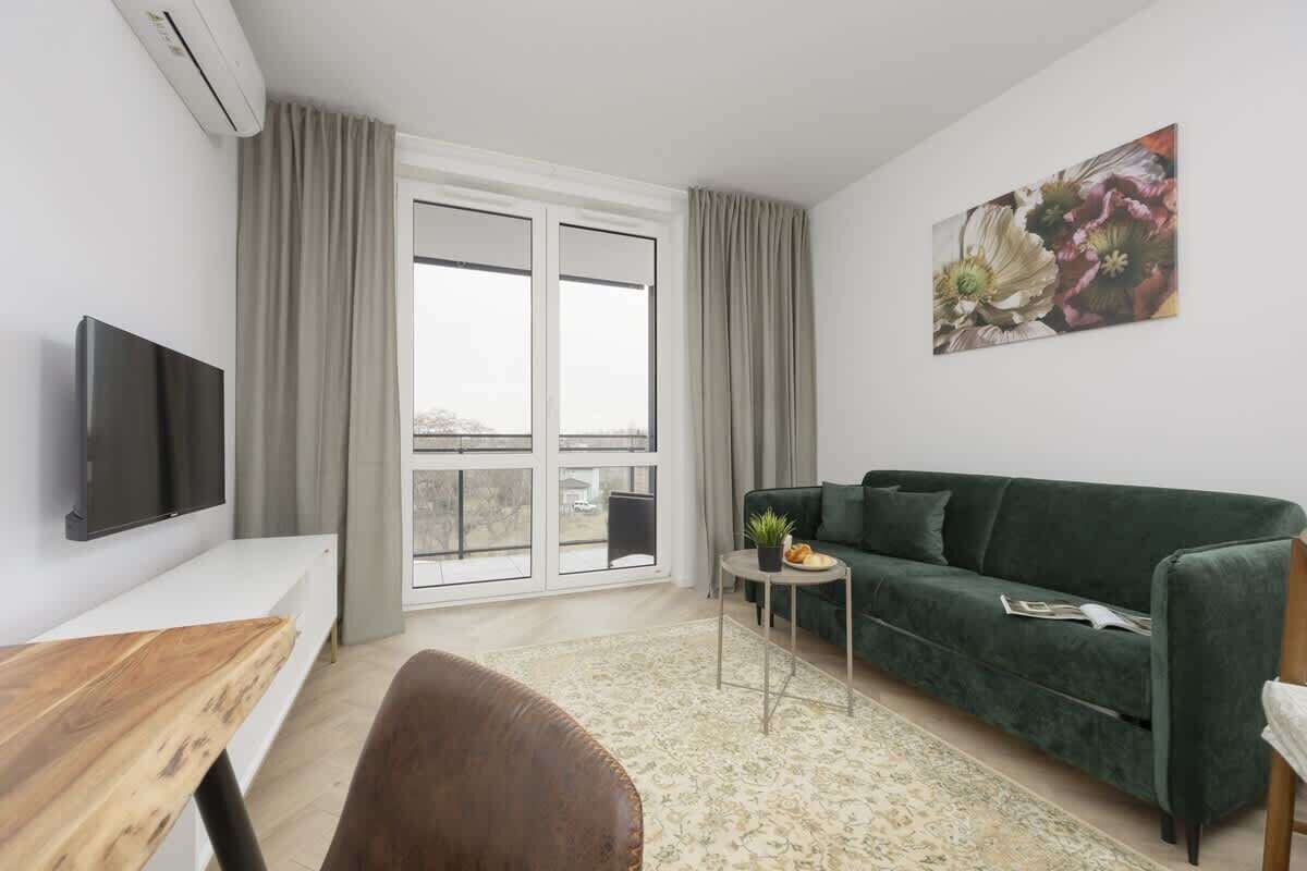 A modern living room with a green sofa, a flat-screen TV, a wooden table, and a small side table with a plant.