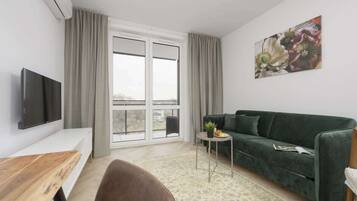 A modern living room with a green sofa, a flat-screen TV, a wooden table, and a small side table with a plant.