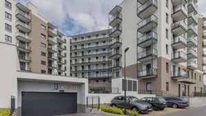 A multi-story residential building with balconies, a parking garage, and a clear sky. - Charming Apartment with Balcony | Close to Chopin Airport (Warszawa)